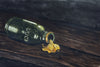 Water color painting of a dark green glass bottle with the word “luck” embossed on the side. Bottle is tipped over, pouring out liquid gold onto a dark wooden table.