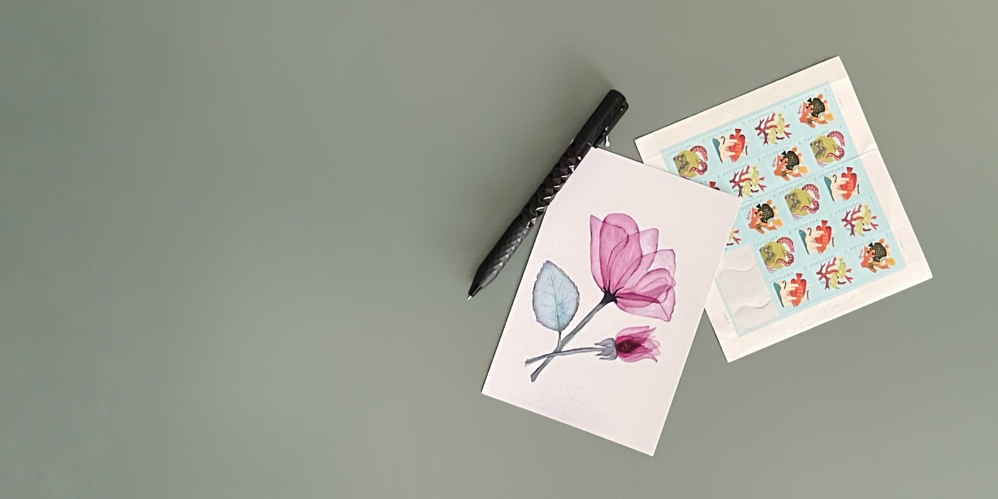 Postcard with transparent tulip artwork sitting next to a page of postcard stamps and a pen