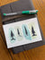 Water color postcard of pine trees on green background sitting on leather notebook.